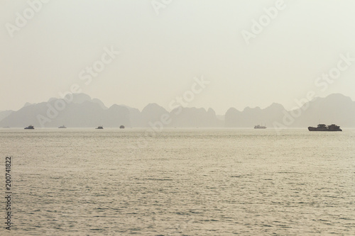 Tourists boats are cruising on the emerald waters with thousands of towering limestone islands in background in golden hour at Quang Ninh, Vietnam