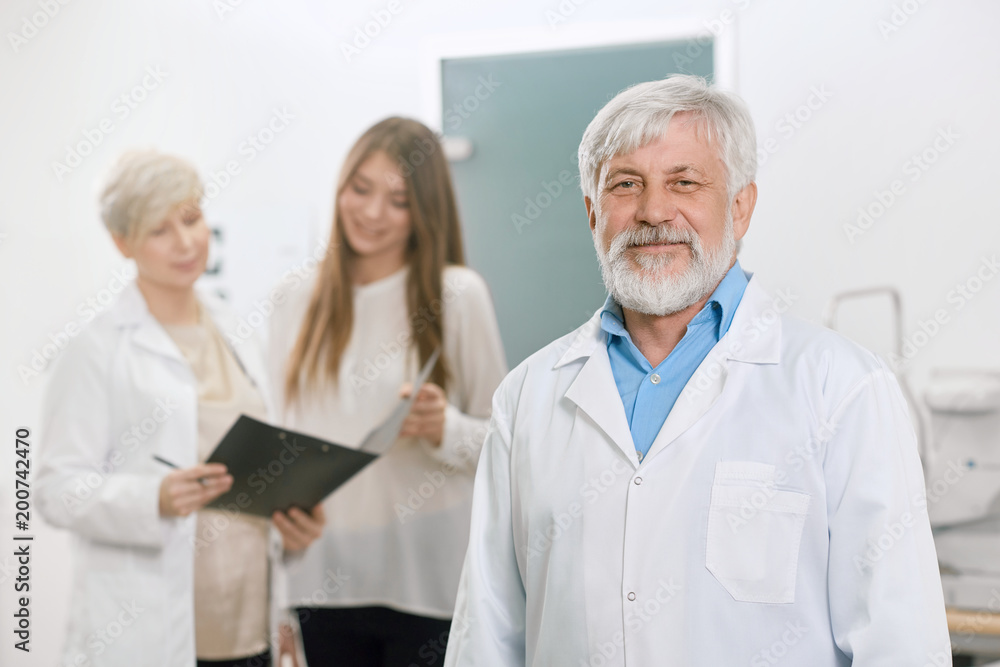 Confident old doctor staying in front of assistant and patient. Looking expirienced, skilled, professional. Working in ophthalmological laboratory gor vision saving and improving. Confident old doctor staying in front of assistant and patient. Looking expirienced, skilled, professional. Working in ophthalmological laboratory gor vision saving and improving.