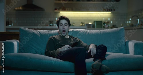 Tired and sleepy man yawning as he  watches tv late at night.