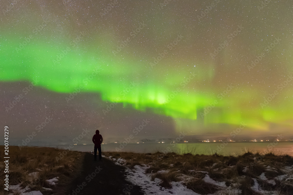 Aurora Borealis (Northern Lights) phenomenon in winter.Photographer standing under Aurora Polaris solar storm above his head at night in iceland