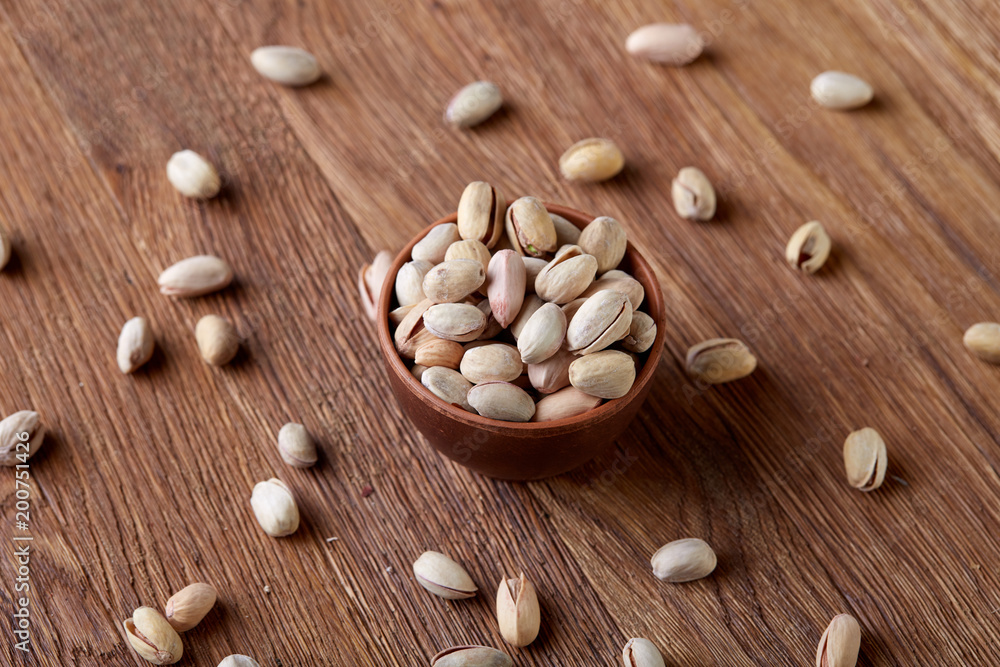 Salted pistachios on a wooden plate over wooden background, top view, close-up, selective focus.