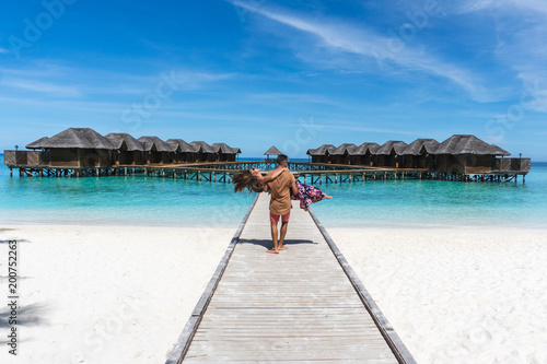 Honeymoon on Maldives. Man holding his wife on arms on bridge on ocean beach