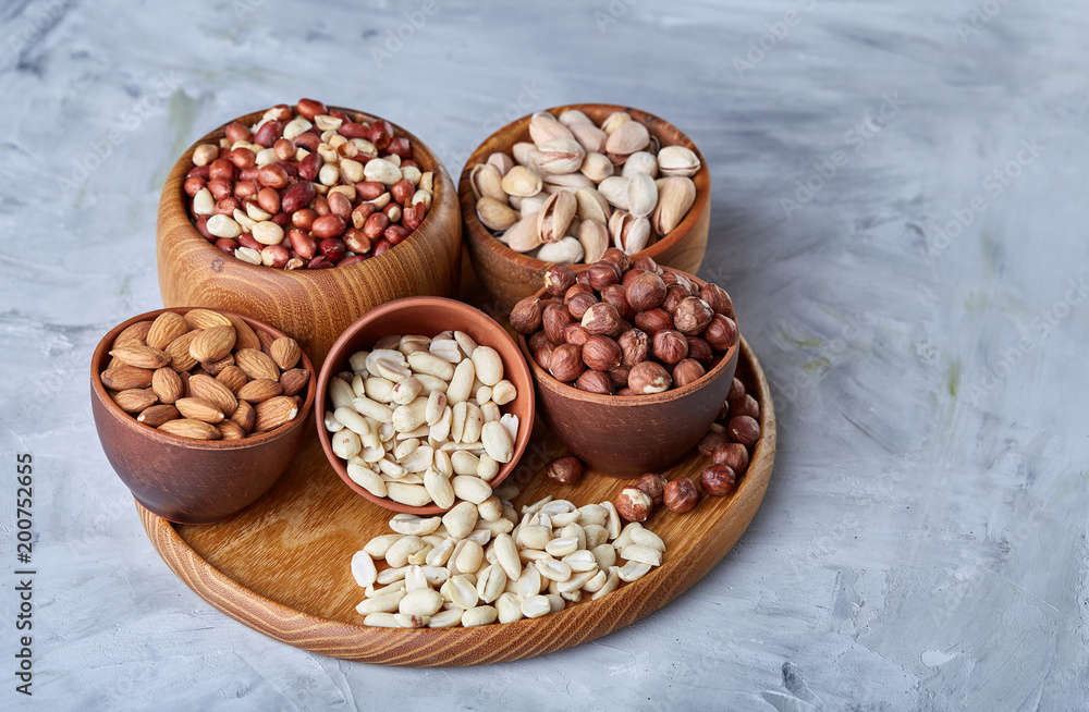 Mixed nuts in brown bowls on wooden tray over white background, close-up, top view, selective focus. Mixed nuts in brown bowls on wooden tray over white background, close-up, top view, selective focus.