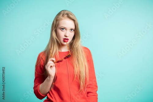 Young beautiful girl with blond hair on a blue background looking at the camera, holding sunglasses