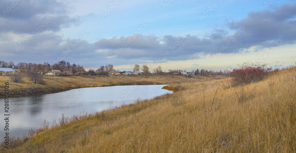 Late autumn.Country landscape with river and village on a  background of ovecast sky.