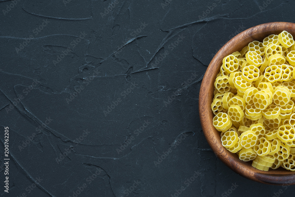 Macaroni ruote pasta in a wooden bowl on a black textured background from  the side. Close-up with the top. Free space for text. Stock Photo | Adobe  Stock