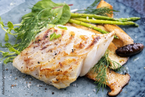 Fried cod fish filet with green asparagus and mushrooms as close up on a plate photo