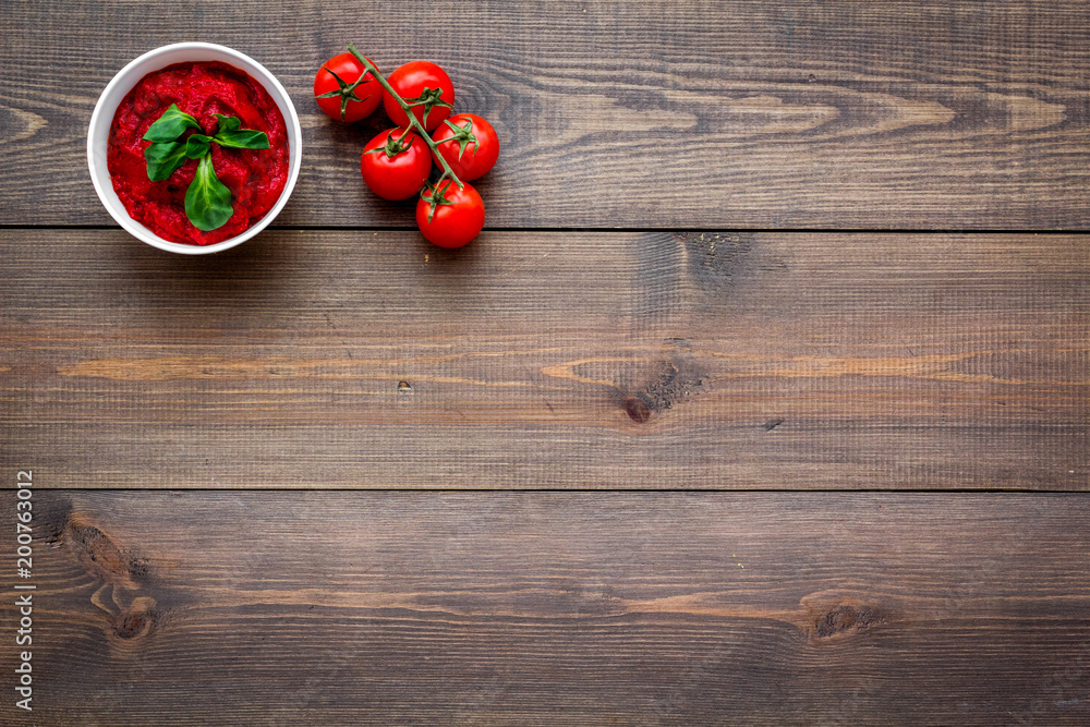 Tomato sauce in bowl with green basil near cherry tomatoes on dark wooden background top view copy space