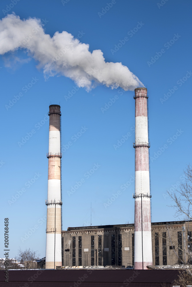 Smoke, air emissions from an industrial pipe against a clear blue sky. Old power station.