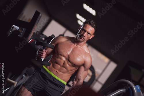 Portrait of handsome fitness model working out with dumbbells. Strong muscular bodybuilder with naked torso posing in gym.