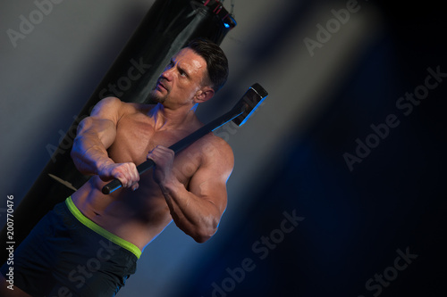 Portrait of Sexy fitness model posing with hard sledgehammer. Muscular strong bodybuilder training in the gym