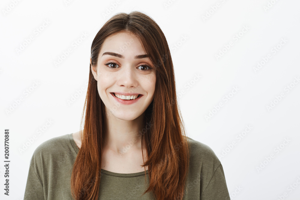 Close-up portrait of good-looking friendly female student in casual outfit, smiling politely, talking casually with customer, offering help while standing against gray background Close-up portrait of good-looking friendly female student in casual outfit, smiling politely, talking casually with customer, offering help while standing against gray background
