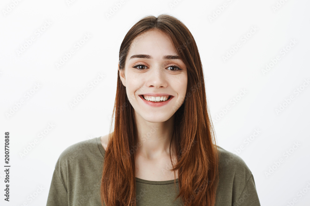Charming joyful adult sister talking about life in university while on holidays at home, standing over gray background and smiling broadly, expressing friendly and happy attitude Charming joyful adult sister talking about life in university while on holidays at home, standing over gray background and smiling broadly, expressing friendly and happy attitude
