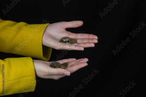 Girl with outstretched hands in which coins, black background, close-up
