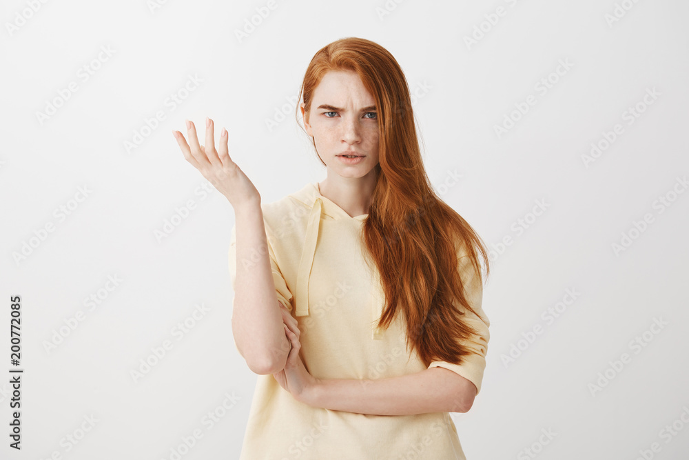 What the hell are you talking about, nonsense. Studio shot of frustrated female with red hair gesturing with raised palm, frowning, being displeased and confused with dumb question over gray wall What the hell are you talking about, nonsense. Studio shot of frustrated female with red hair gesturing with raised palm, frowning, being displeased and confused with dumb question over gray wall