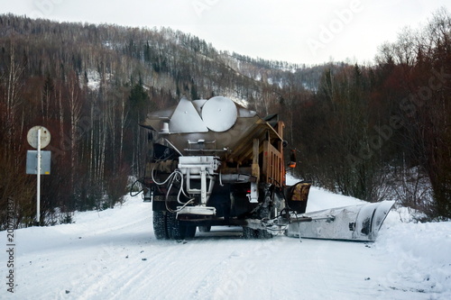 The snow-removing machine cleans the road from the snow in the background of the mountain taiga.