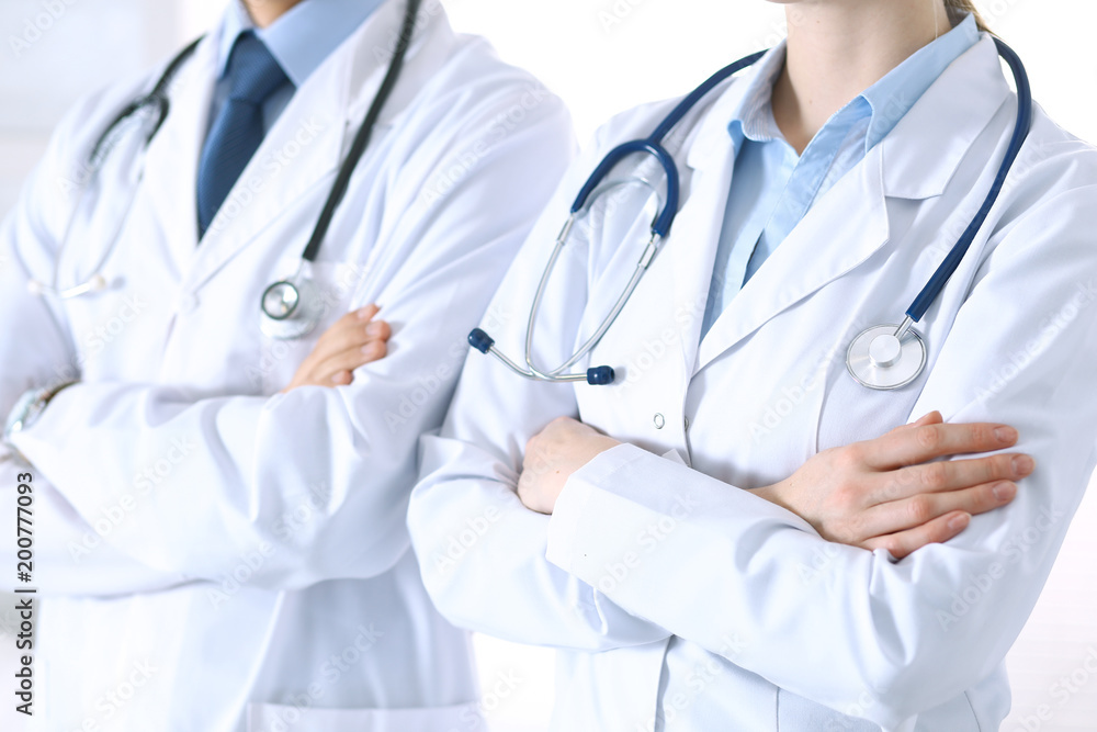 Team of unknown doctors standing straight with arms crossed in hospital. Physicians ready to help. Healthcare, insurance and medicine concept Team of unknown doctors standing straight with arms crossed in hospital. Physicians ready to help. Healthcare, insurance and medicine concept