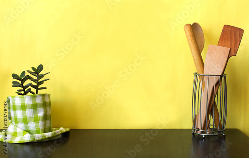 Kitchen utensils and house plant on dark shelf over yellow wall. Kitchen interior background with copy space