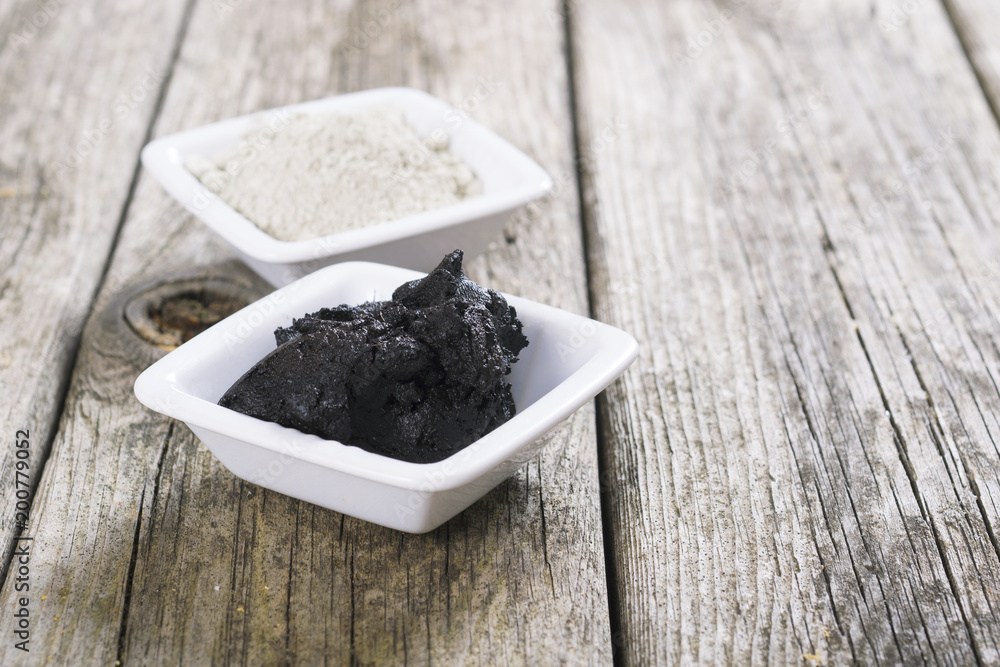 gray cosmetic clay powder and black mud on old wood texture