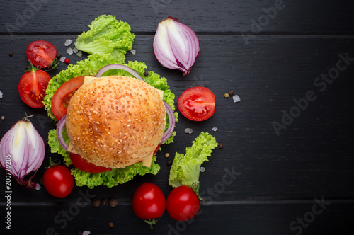 Beef burgers with vegetables. Lies on black textured background with lettuce, tomatoes and spices. Top view