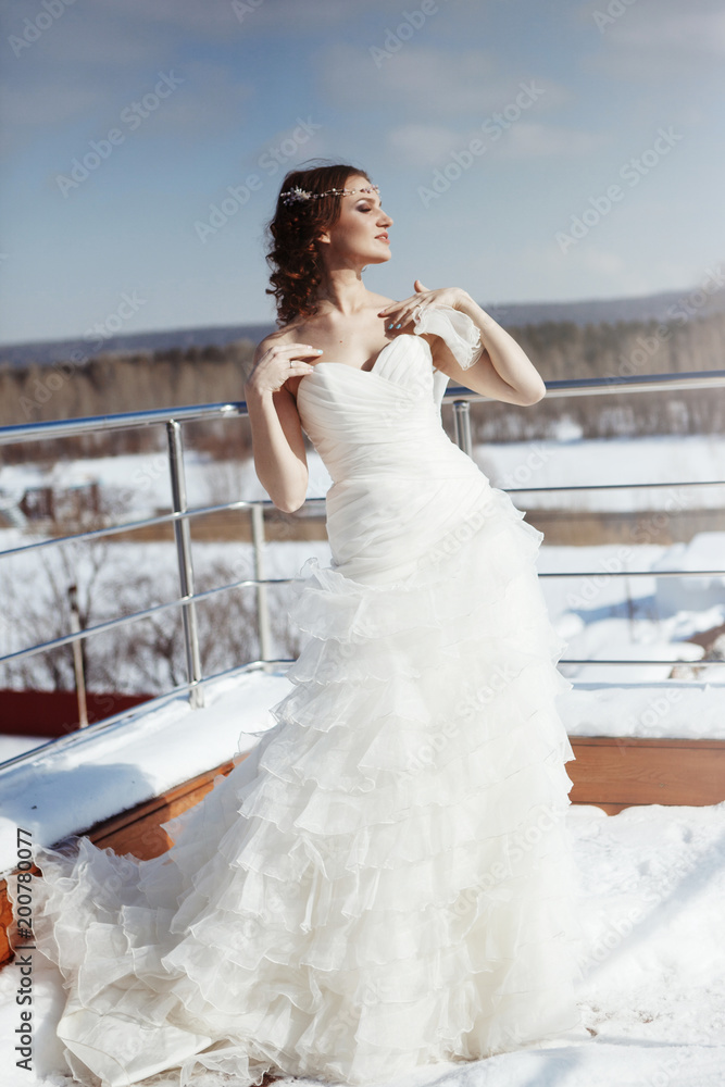 Cute young bride in white wedding dress with diadem in hair outdoors in winter Cute young bride in white wedding dress with diadem in hair outdoors in winter