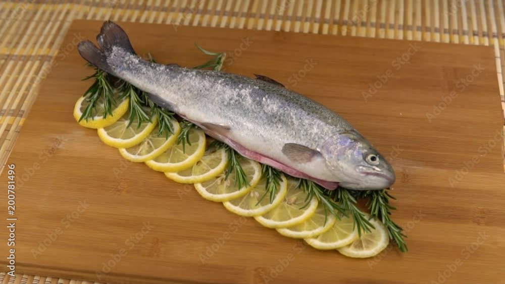 Preparation of trout, sliced lemon and green rosemary. Cooking food on a wooden board Preparation of trout, sliced lemon and green rosemary. Cooking food on a wooden board
