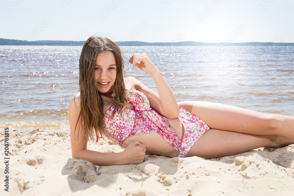 Outdoor shot of smiling young female model girl in bikini lying