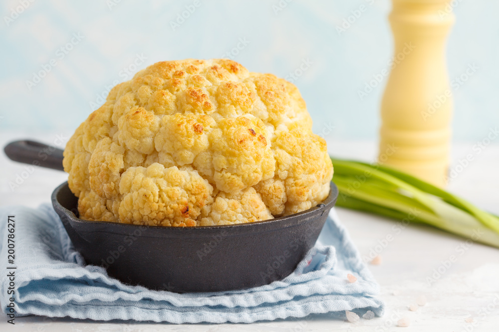 Whole baked cauliflower in a cast-iron frying pan, light background. Healthy vegan food concept. Whole baked cauliflower in a cast-iron frying pan, light background. Healthy vegan food concept.