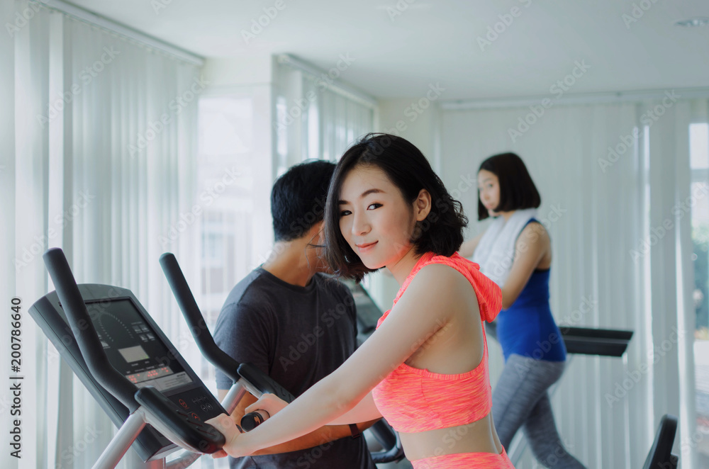 asian young woman slim body exercising on bicycle machine with young man personal trainer in fitness gym, bodybuilder, healthy lifestyle, fitness, workout and sport training concept, soft focus
