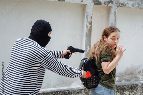 thief in black and white jacket with gun in hand stealing the wallet or mobile phone from behind young caucasian woman traveling bag on street in big city, thief, crime, robber and steal concept photo