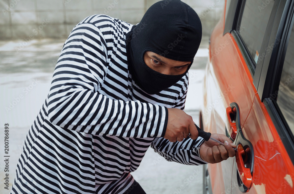 thief in black and white jacket using screwdriver to open car door to stealing a car on street in big city, break into the car crime robber and steal concept