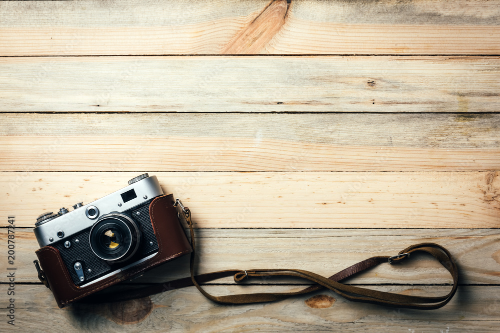 Old vintage film photo camera with brown leather strap on grunge wooden table. Photographe concept background