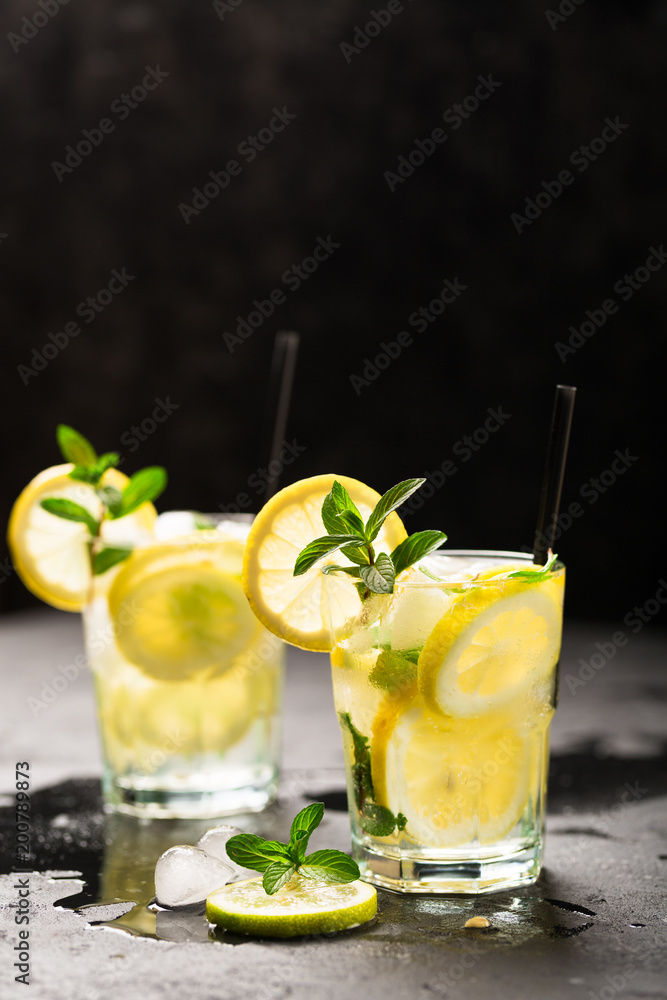 Fototapeta premium Lemon fruit lime slices caipirinha from Brazil, lemonade mint ice cubes in cold glasses on dark background, alcoholic mojito cockail ice tea green mint leaves, brown sugar spoon, copy space