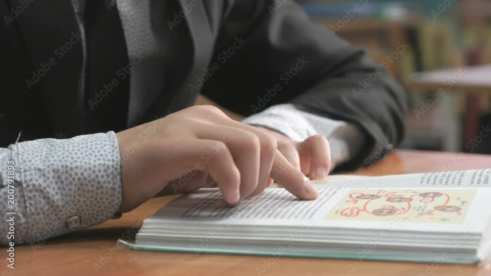 Unknown schoolboy dressed in black suit sitting at a table and reading a book. Close-up Unknown schoolboy dressed in black suit sitting at a table and reading a book. Close-up