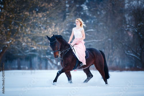 Young woman in pink dress galloping horseback on winter field. Romantic or historical equestrian background with copy space
