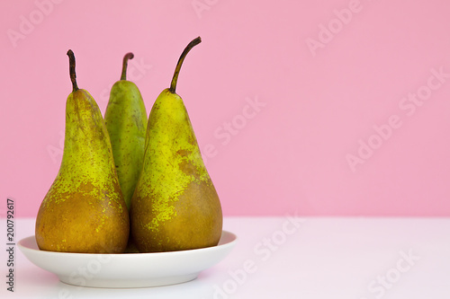 three ripe long pears on a saucer on a creative pink background