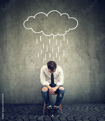 Sad business man sitting on a chair looking down with a rain cloud above him photo