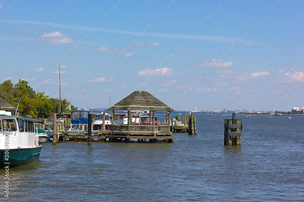 A pier at waterfront of Old Town Alexandria, Virginia, USA. A wooden gazebo and views over the Potomac River with US capital on horizon.