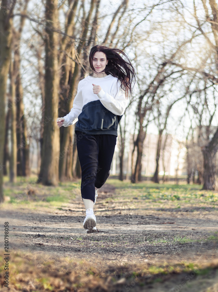 Woman runner running through the spring park road. Woman runner running through the spring park road.