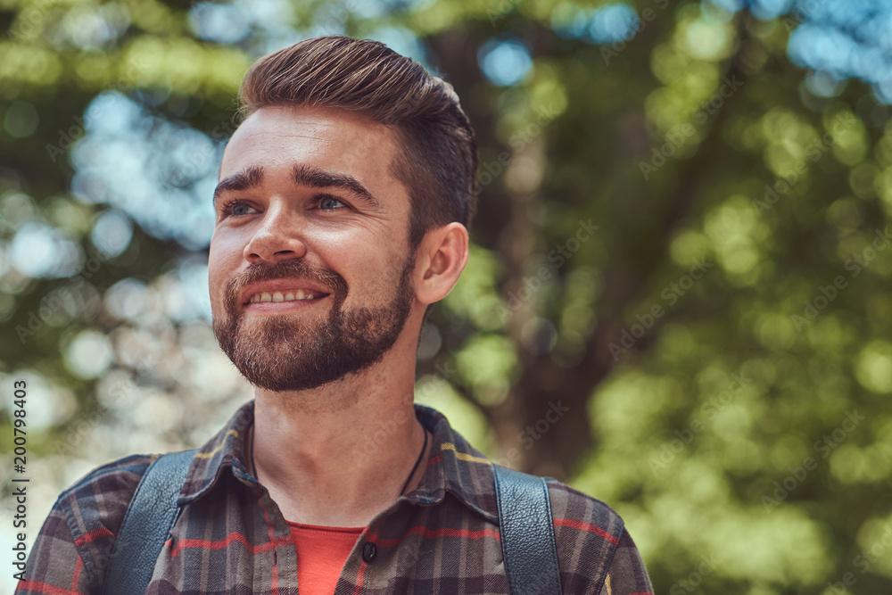 Close-up portrait of a smiling young beautiful student with stylish haircut and beard, wearing a fleece shirt, standing in the park. Close-up portrait of a smiling young beautiful student with stylish haircut and beard, wearing a fleece shirt, standing in the park.
