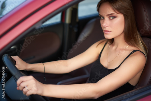 Concept: strong independent young woman in car. Beautiful serious girl sit behind the wheel at twilight. Outside look.