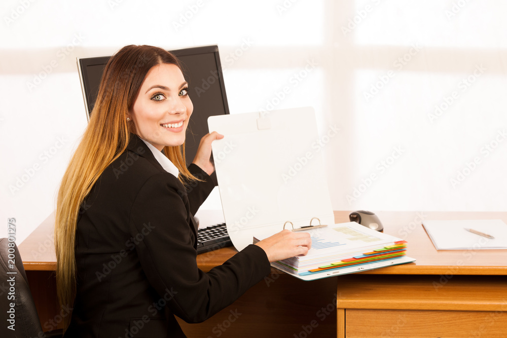 Young business woman with bold folder checking data at her desk in the office Young business woman with bold folder checking data at her desk in the office