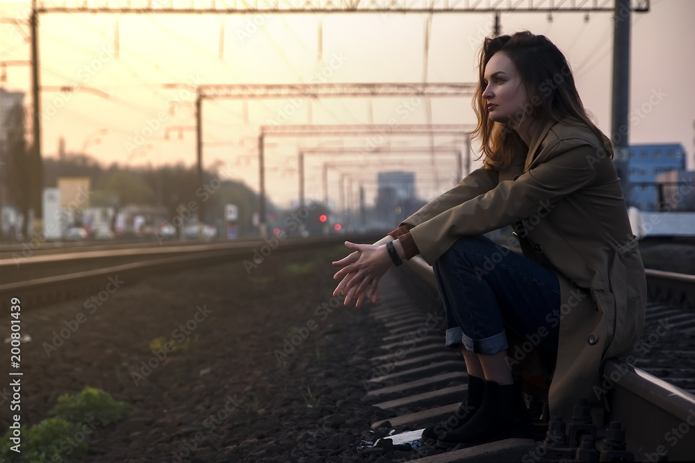 A young girl sits on the rails on a warm summer evening