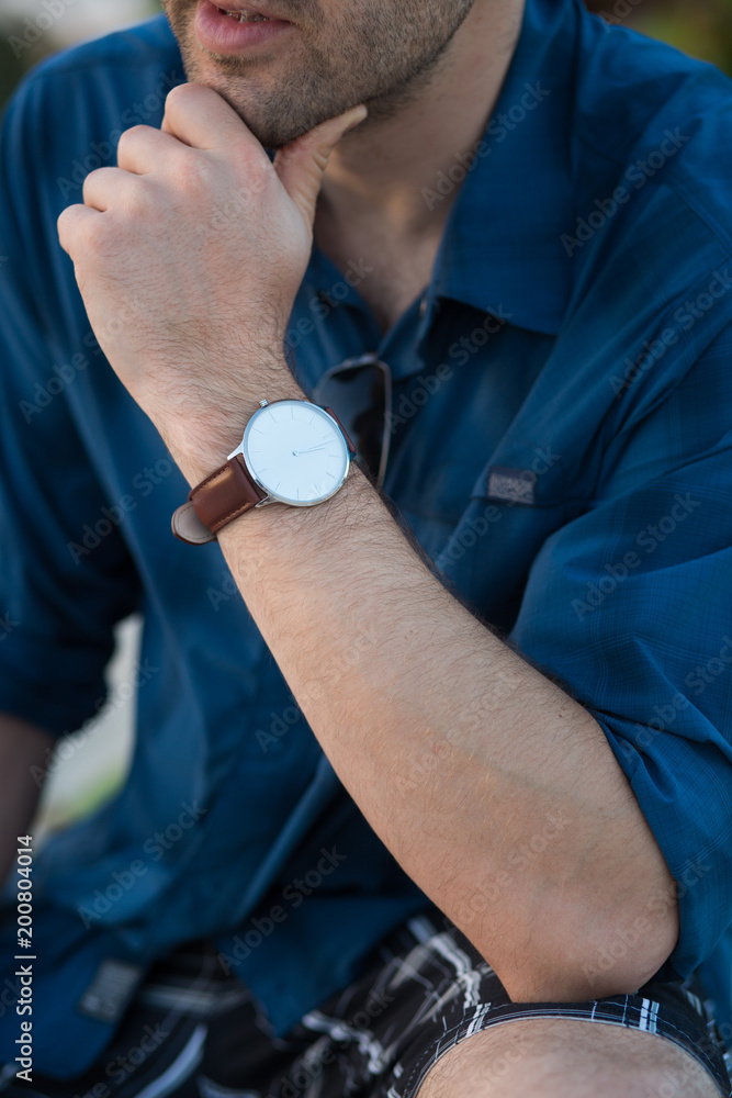 A man in a casual posture, wearing a wristwatch on his arm and thinking