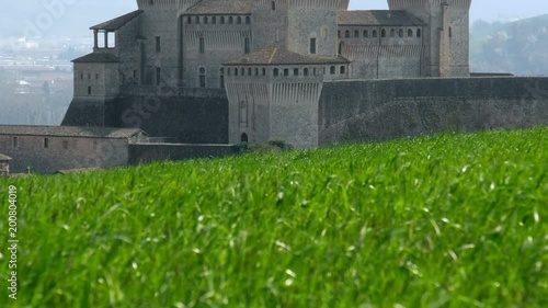 castle of Torrechiara in Parma, Italy through windy meadow grass panorama - Emilia Romagna region vertical panning photo