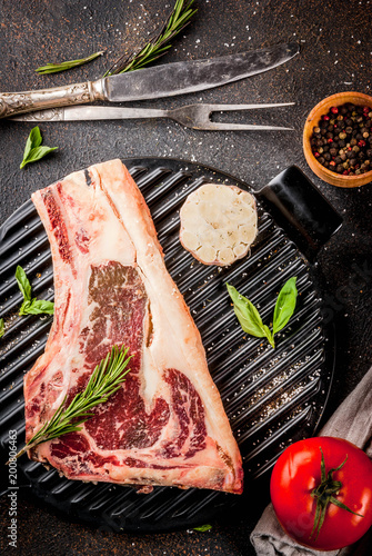 Raw beef marbled meat striplon rib eye steak with spices, grill pan, and herbs, dark background top view, copy space photo