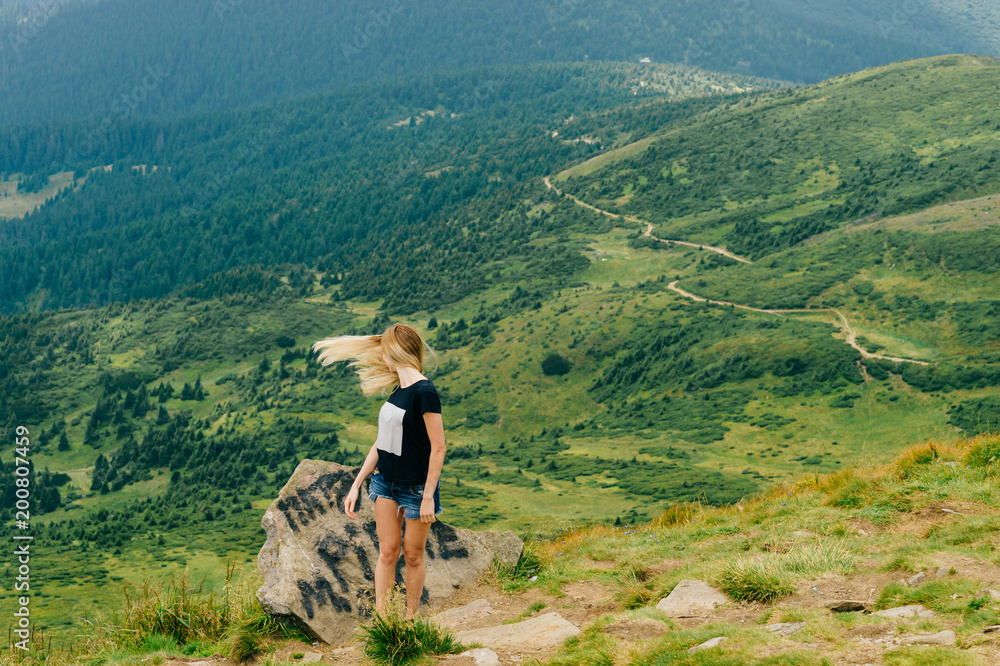 Young beautiful odd blonde girl mood portrait.  Unusual female person with flying hair in motion. Traveler cute babe strange gestures. Tourist woman at top of mountain enjoying freedom and relaxing.