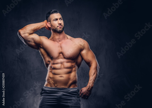 Portrait of a shirtless tall huge male with a muscular body with a stylish haircut and beard, in a sports shorts, posing in a studio.