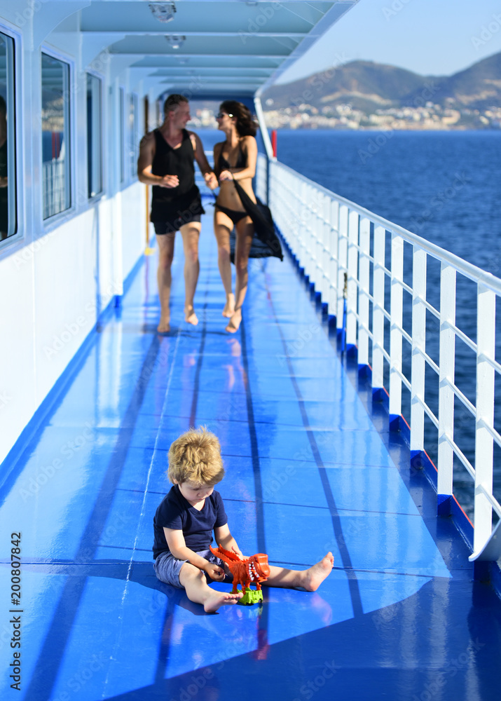 Family travelling on cruise ship, defocused. Family rest concept. Father, mother walk on deck of cruise liner while kid playing with toy, landscape on background. Happy family on summer vacation.
