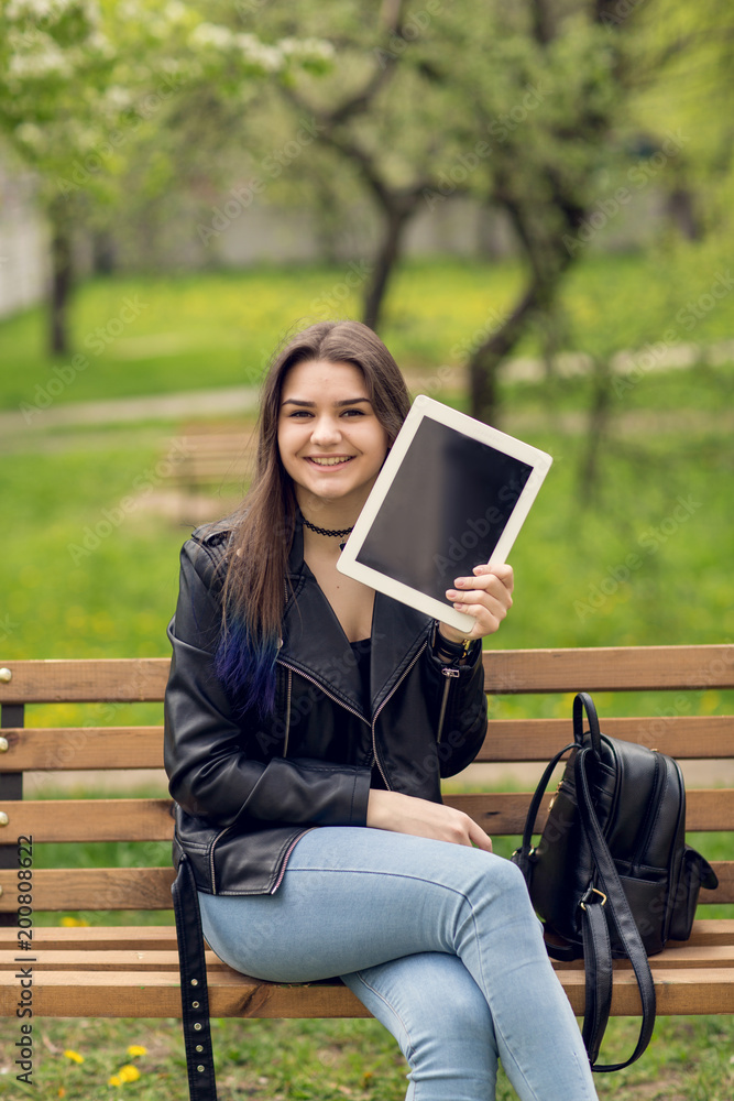 Fototapeta premium Portrait of young girl holding digital tablet in the park